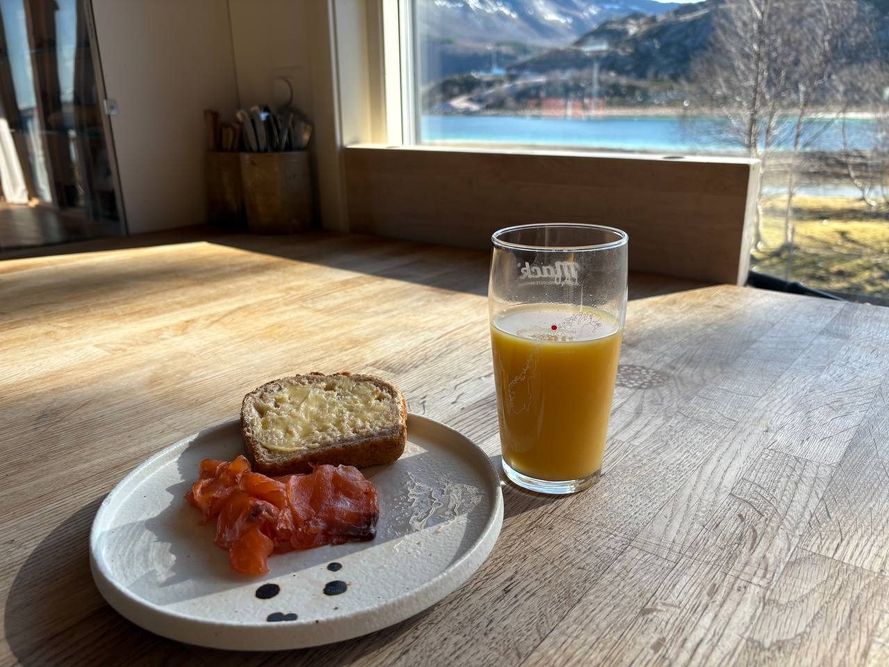 Talíř s uzeným lososem, avokádem a okurkou, v pozadí okno s výhledem na fjord