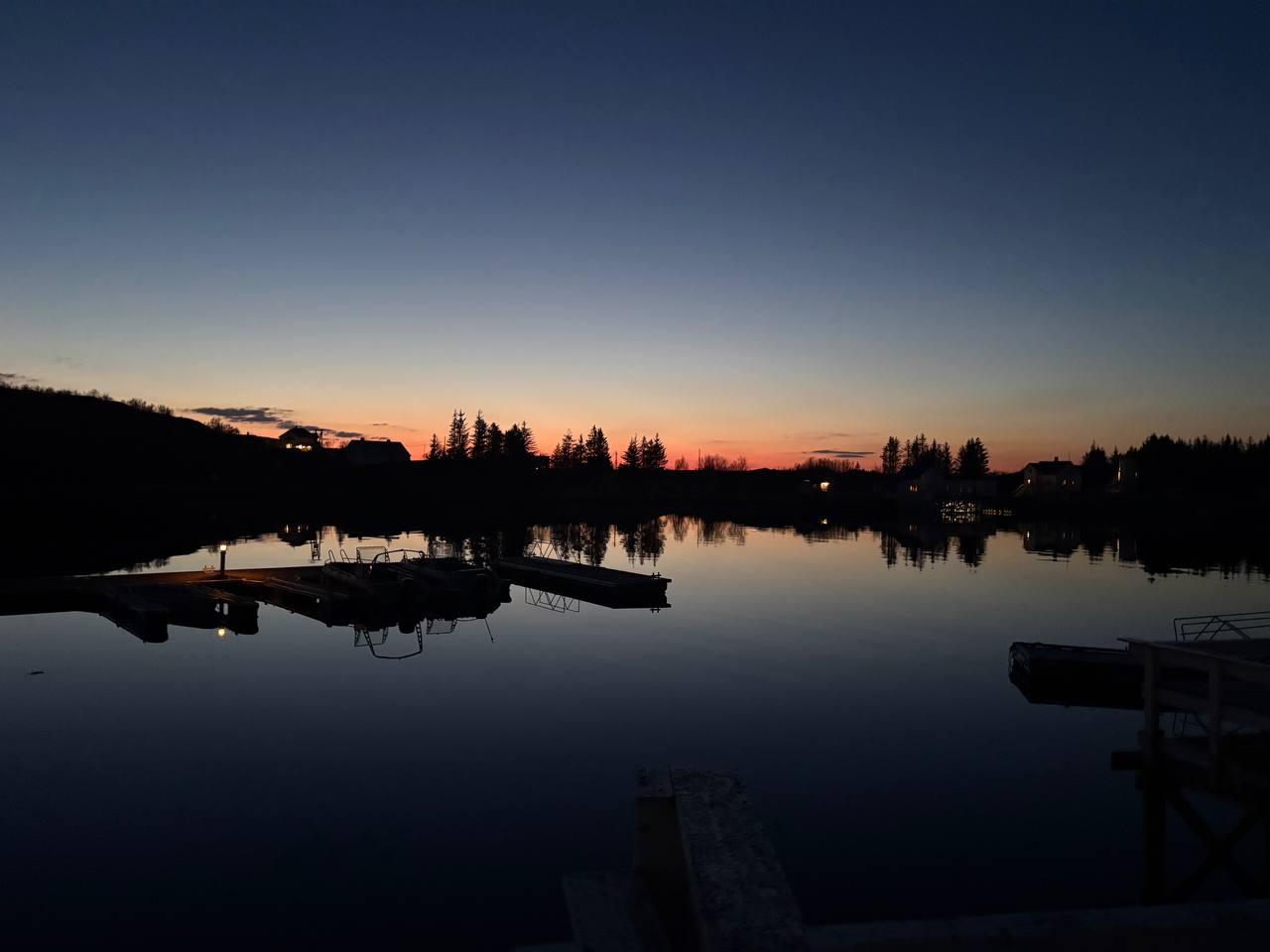 Pohled z mola na fjord po západu slunce, oranžový pruh na obzoru, klidná hladina