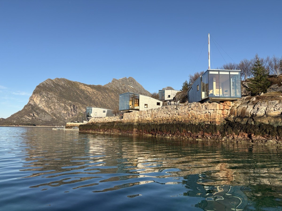 Kabiny Manshausenu na skalách nad průzračně modrým mořem, hory v pozadí