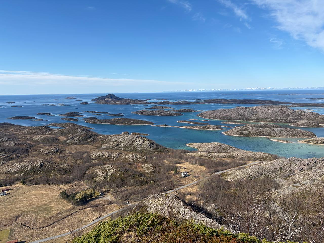 Panoramatický výhled z výšky na desítky skalnatých ostrůvků v tyrkysové vodě, zasněžené hory na obzoru