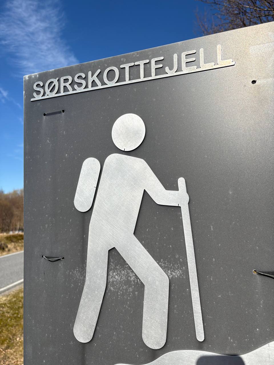 Turistická značka s ikonou chodce na pozadí jarní krajiny a modrého nebe