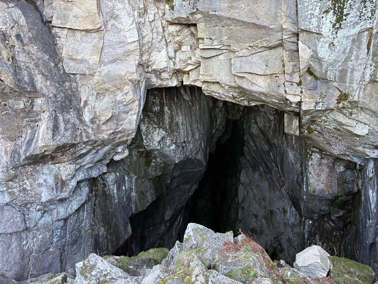 Vstup do jeskyně ve skalním útesu, mechem porostlé balvany