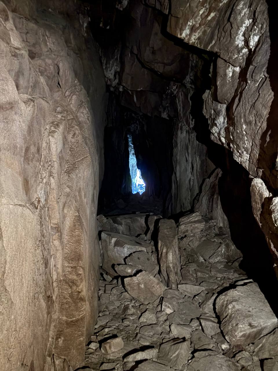 Úzká chodba uvnitř jeskyně, vysoké kamenné stěny, proužek modrého nebe nahoře