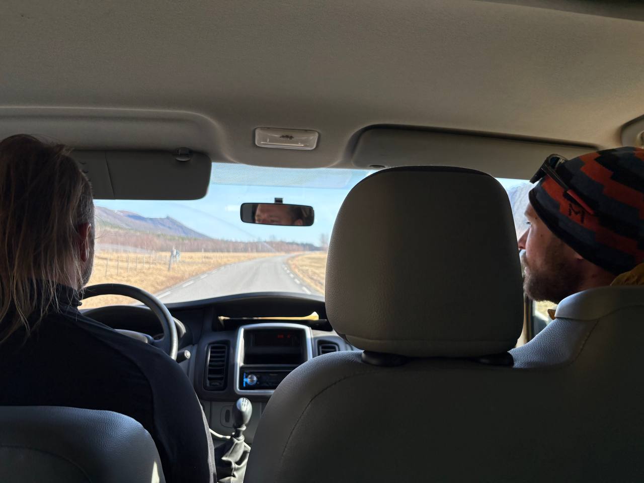 Pohled z auta na prázdnou silnici, hory v dálce, dva lidé vpředu