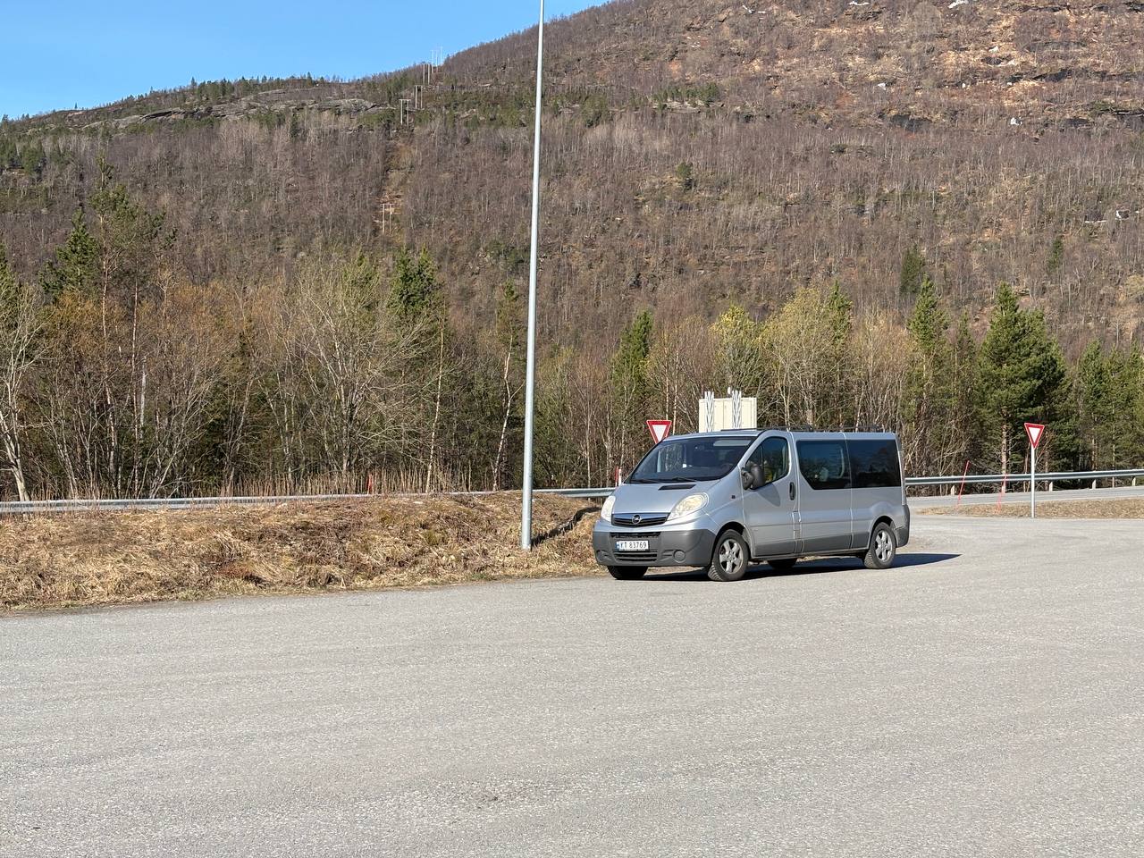 Stříbrná dodávka na parkovišti, zalesněné kopce v pozadí